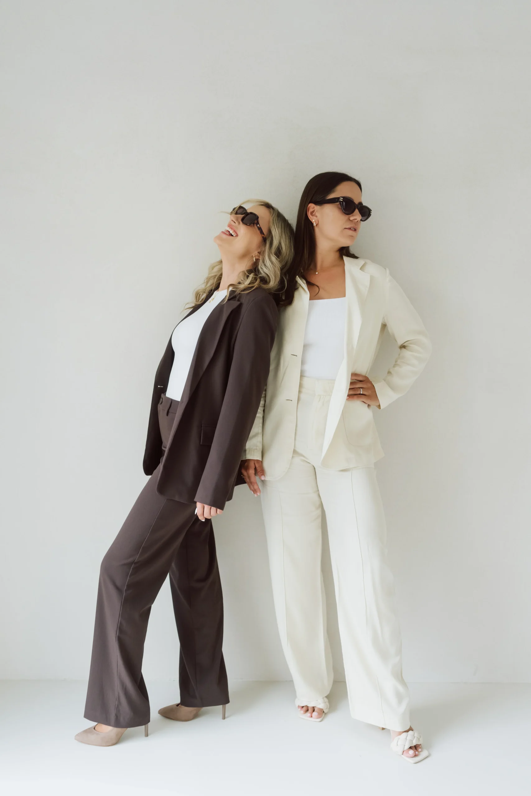Michèle und Giuliana lachend mit Sonnenbrille posieren vor hellem Hintergrund.