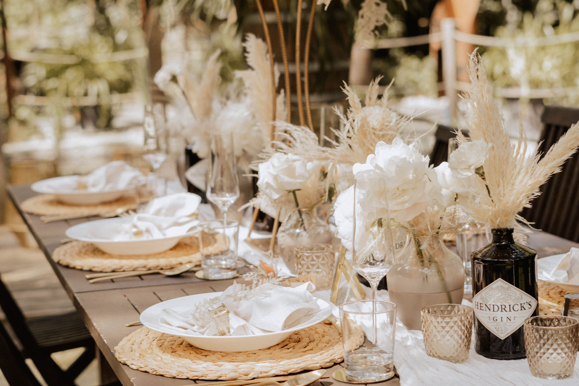 Elegante Boho-Hochzeitstafel mit weissem Geschirr, Naturmaterialien, Gläsern und cremefarbener Blumendekoration.