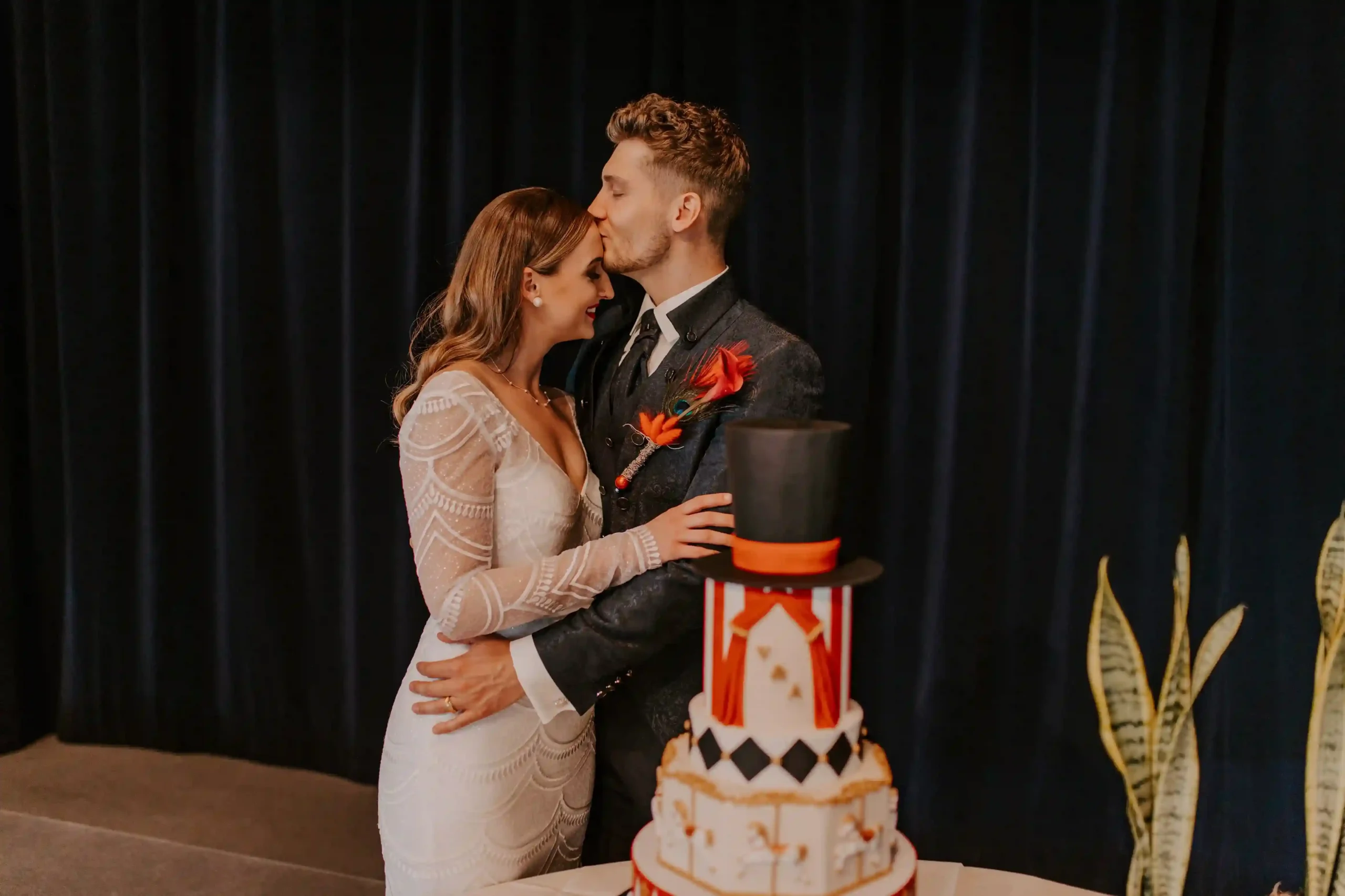Brautpaar steht vor einer mehrstöckigen Hochzeitstorte mit rot-weissen Zirkusmotiven und einem kleinen Zylinder als Tortendekoration.