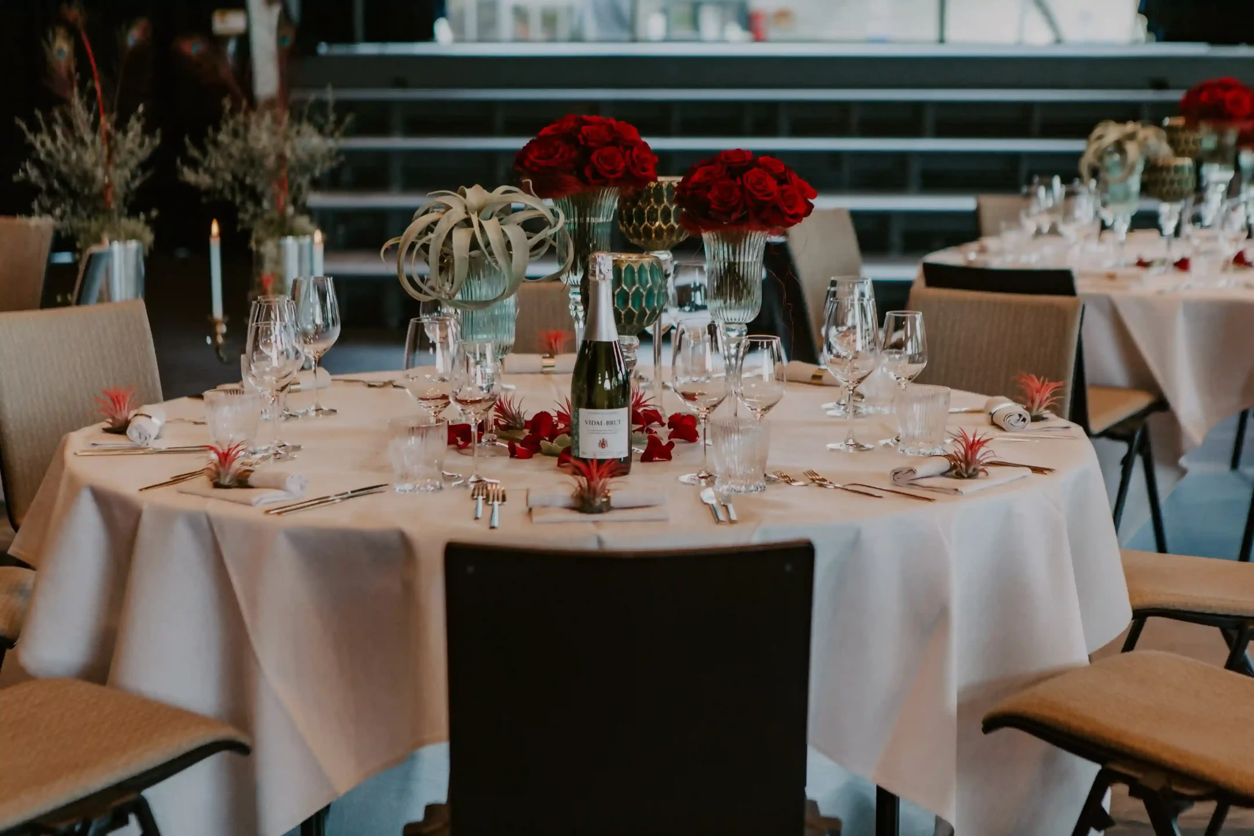 Elegant gedeckter Hochzeitstisch mit weisser Tischwäsche, Glasvasen, roten Blumen und liebevoll arrangierten Dekorationselementen.