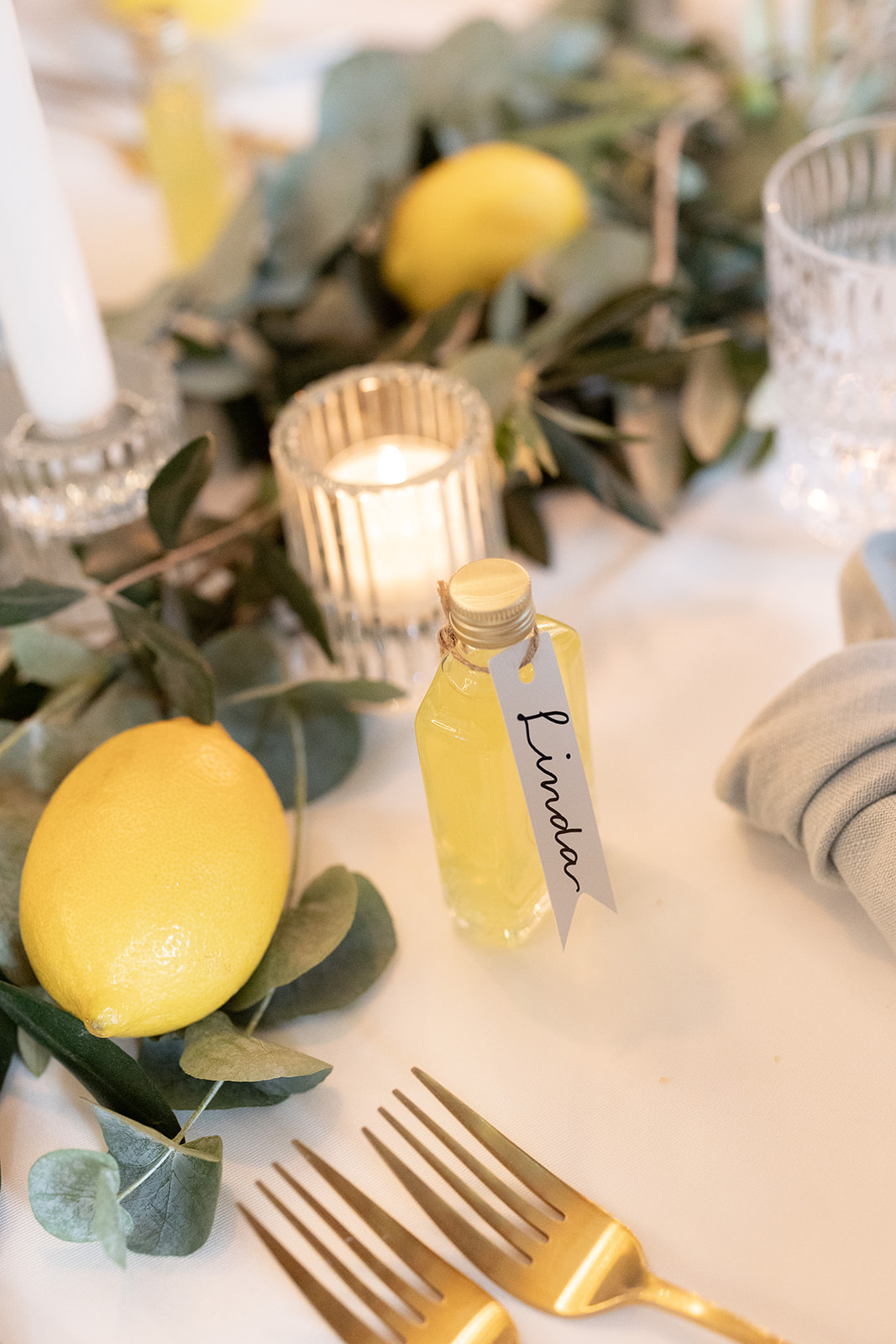 Hochzeitstisch mit gelber Zitrone, Kerzenlicht, floralen Details und einer kleinen Limoncello-Flasche.