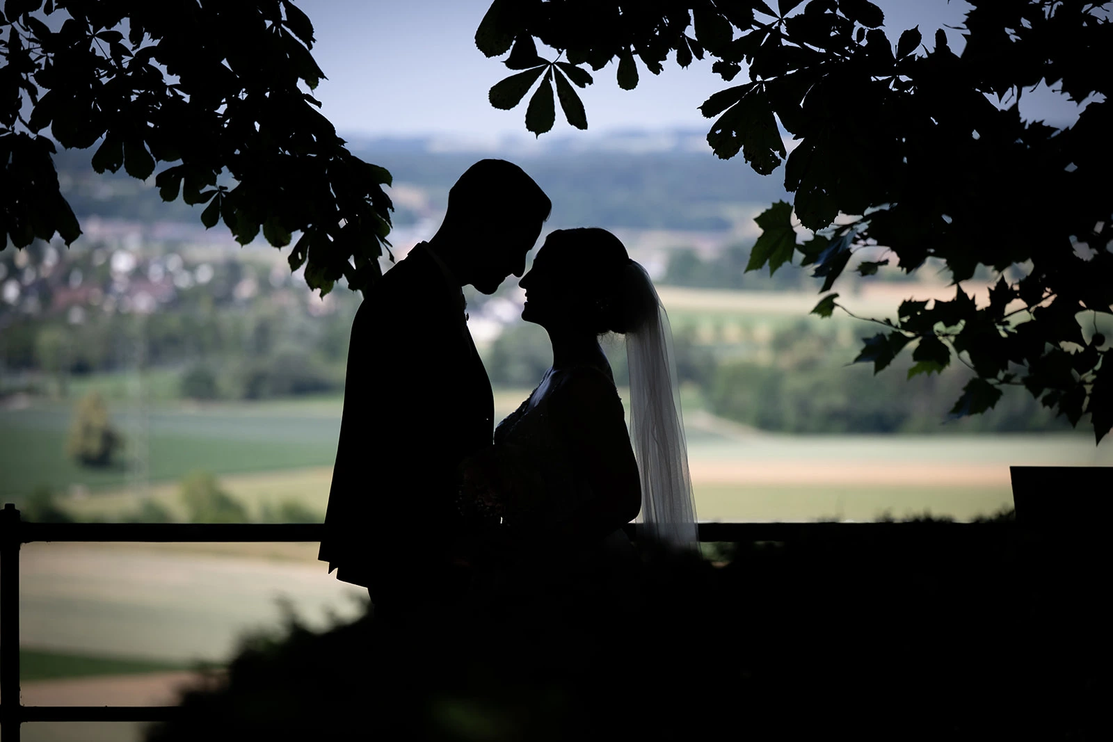 Silhouette von Valentina und Giacomo bei einem Kuss unter Bäumen mit Blick auf die Landschaft.