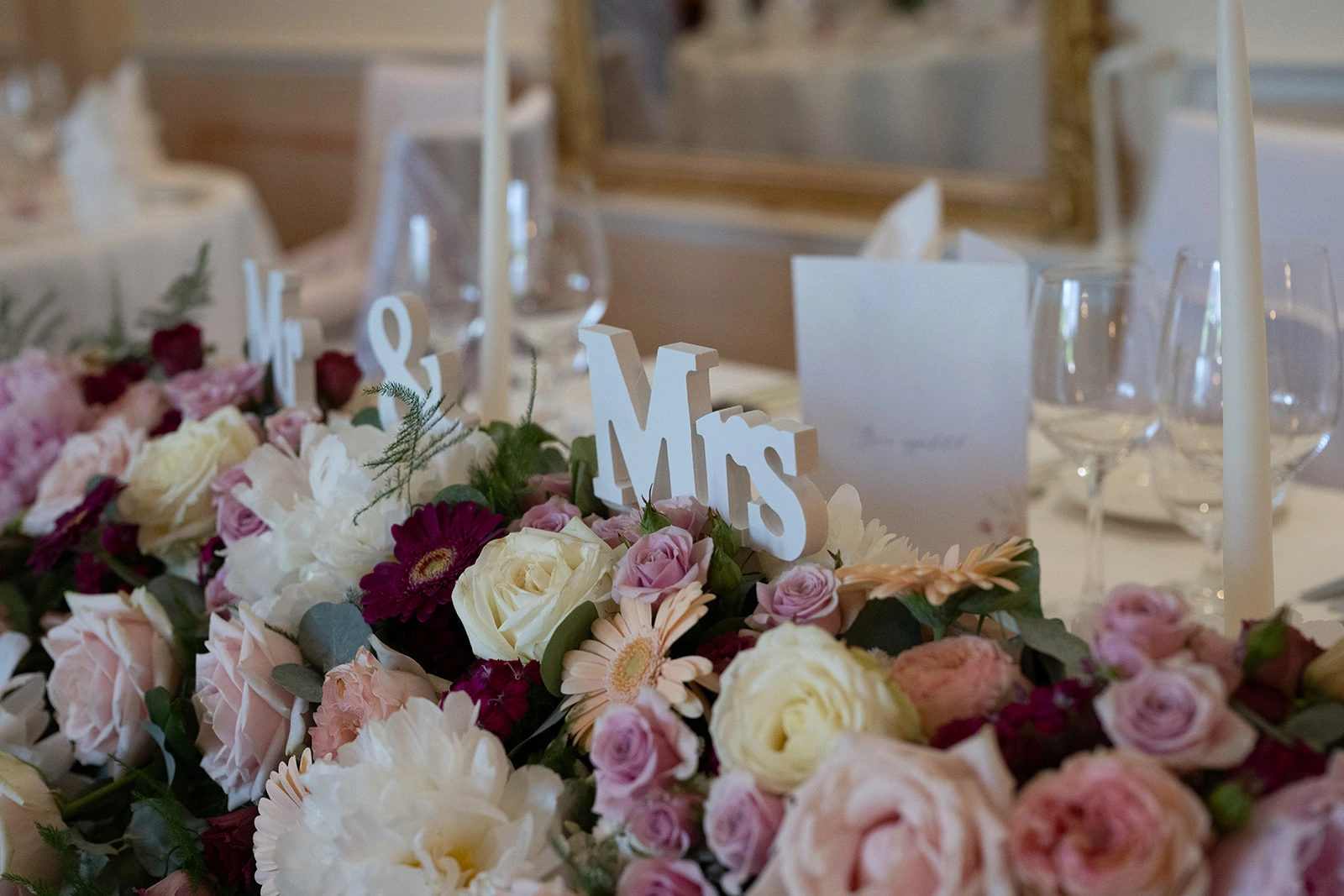 Weisser Mr-&-Mrs-Schriftzug zwischen rosa und cremefarbenen Rosen auf einem Hochzeitstisch.