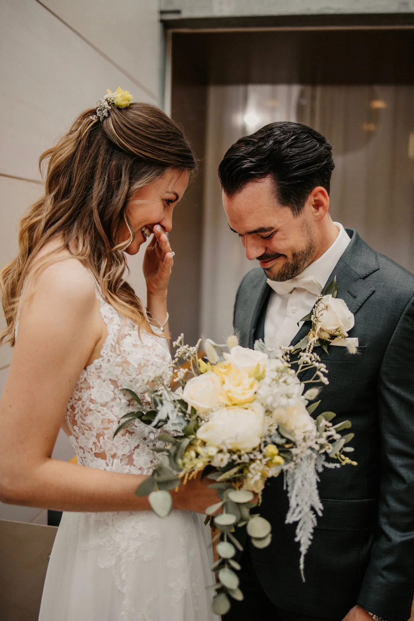 Céline und Philippe lächeln sich während ihrer Hochzeit an. Céline hält einen Brautstrauss mit weissen und gelben Blumen.