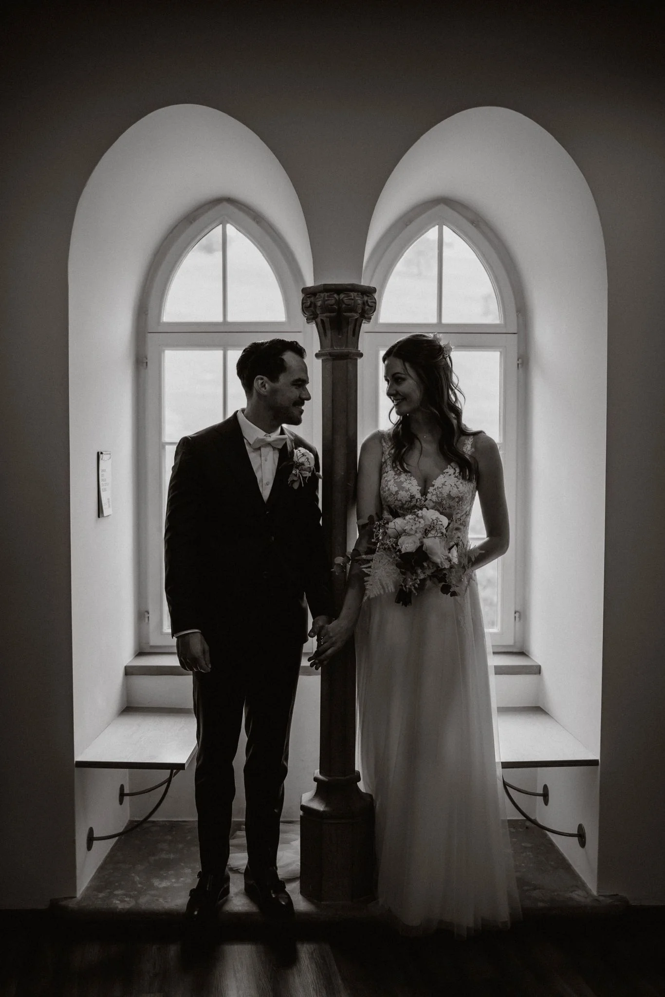 Schwarz-Weiss-Portrait von Céline und Philippe, die gemeinsam vor einem hohen Rundbogenfenster stehen.