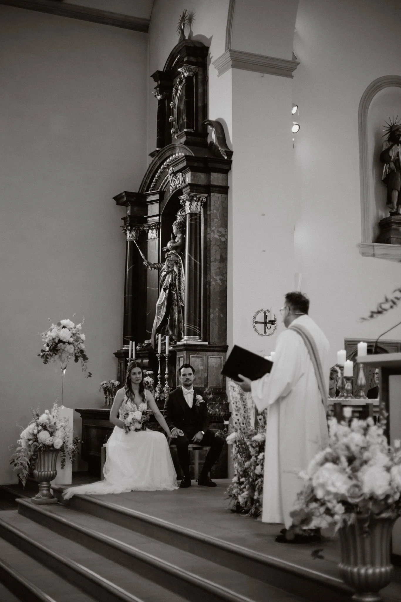 Schwarz-Weiss-Aufnahme der kirchlichen Trauung von Céline und Philippe mit dem Priester vor einem historischen Altar.