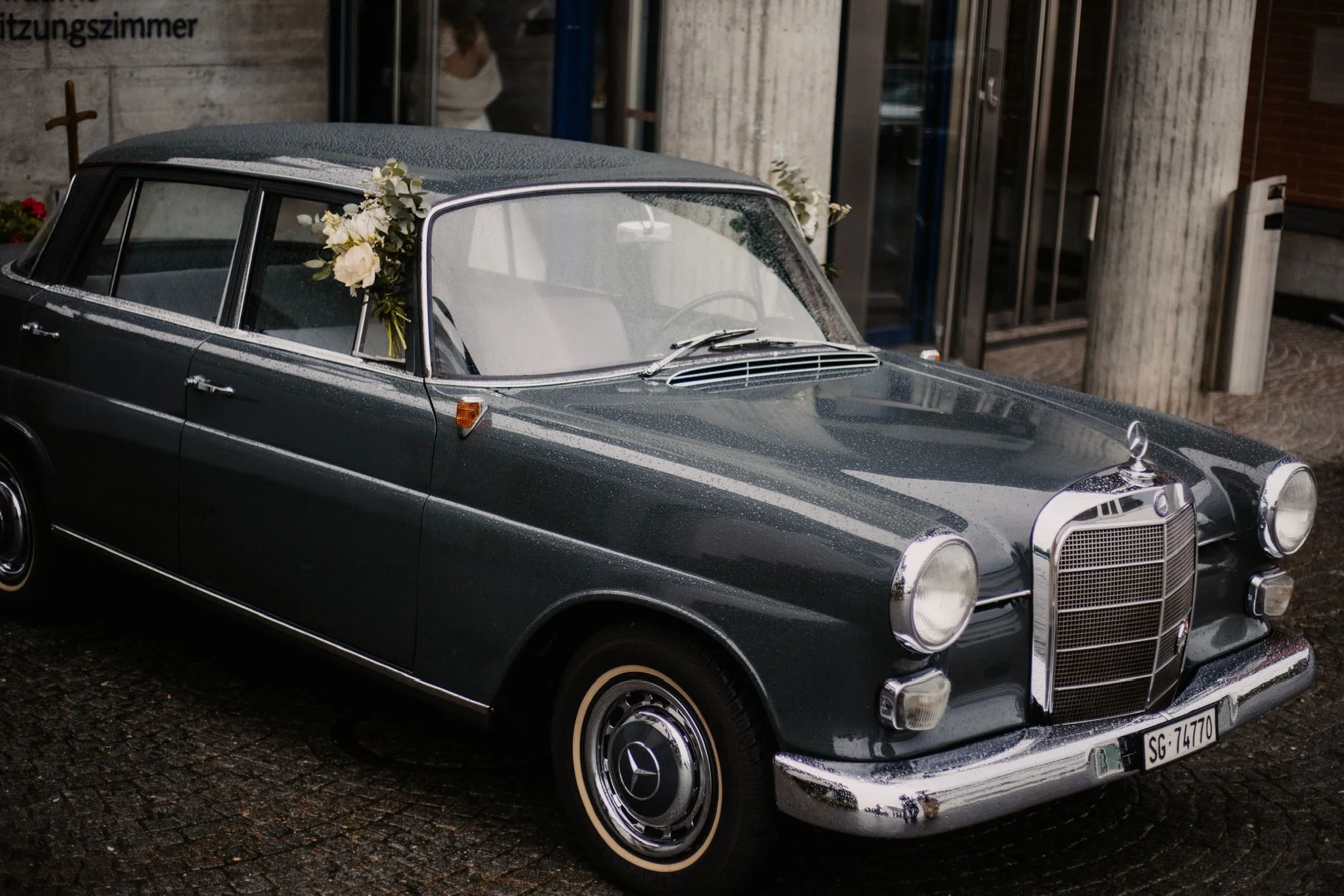 Dunkler klassischer Oldtimer mit Chromdetails steht vor einem historischen Gebäude.