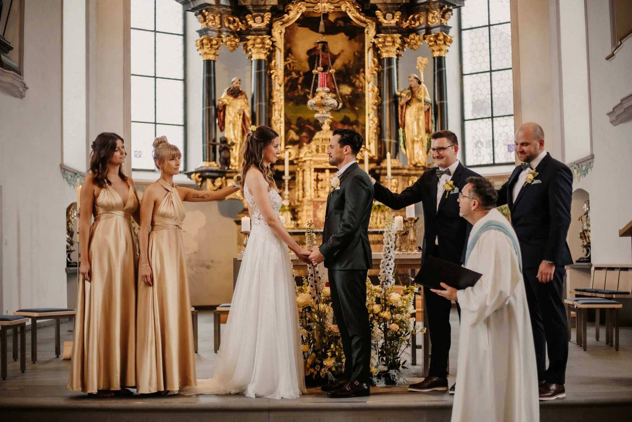 Céline und Philippe stehen mit weiteren Personen vor dem reich verzierten Altar während ihrer kirchlichen Trauung.