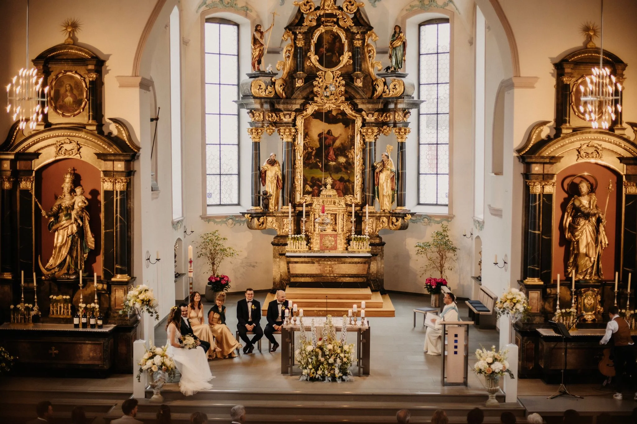 Blick durch den Kirchenraum auf den reich verzierten Hochaltar und die versammelte Hochzeitsgesellschaft.