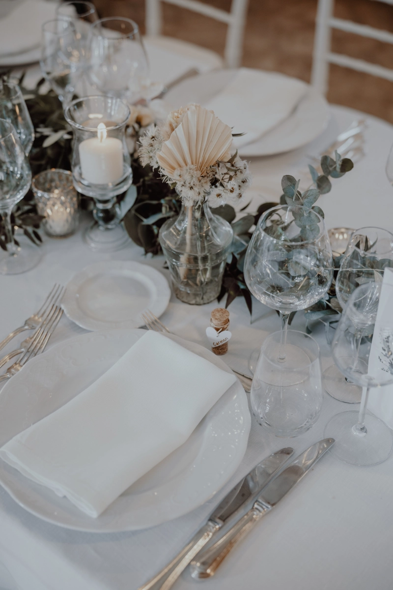 Eleganter Hochzeitstisch mit weissem Geschirr, Gläsern, Servietten und floraler Dekoration.